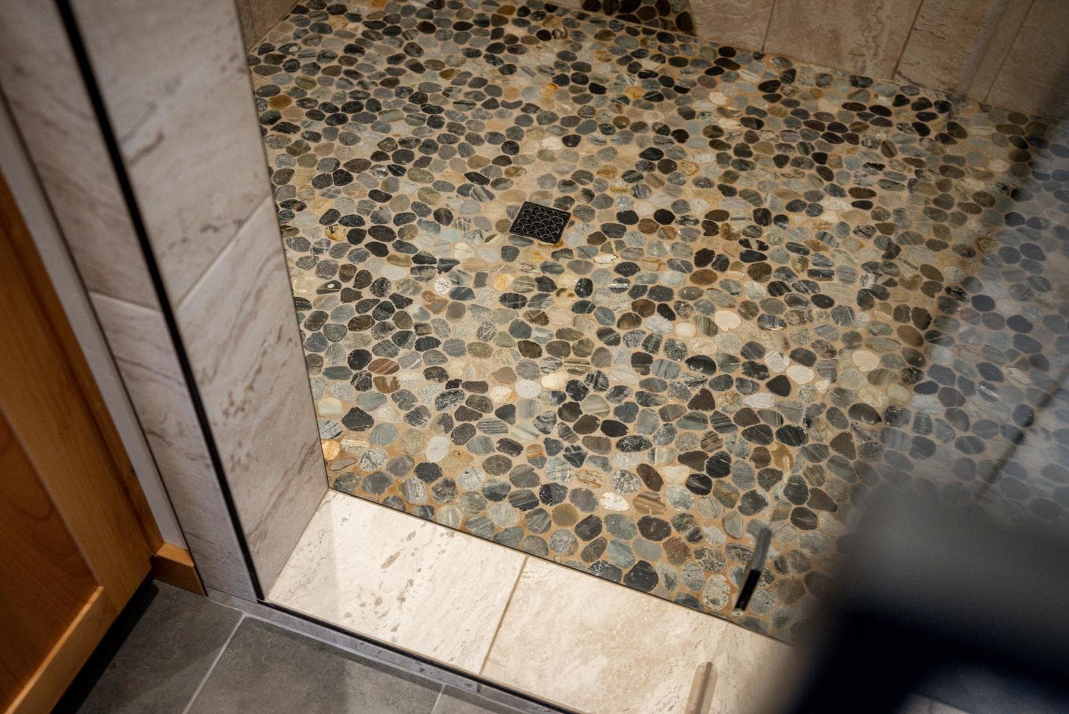 Walk-in tiled shower with river rock style accent tile and floor.