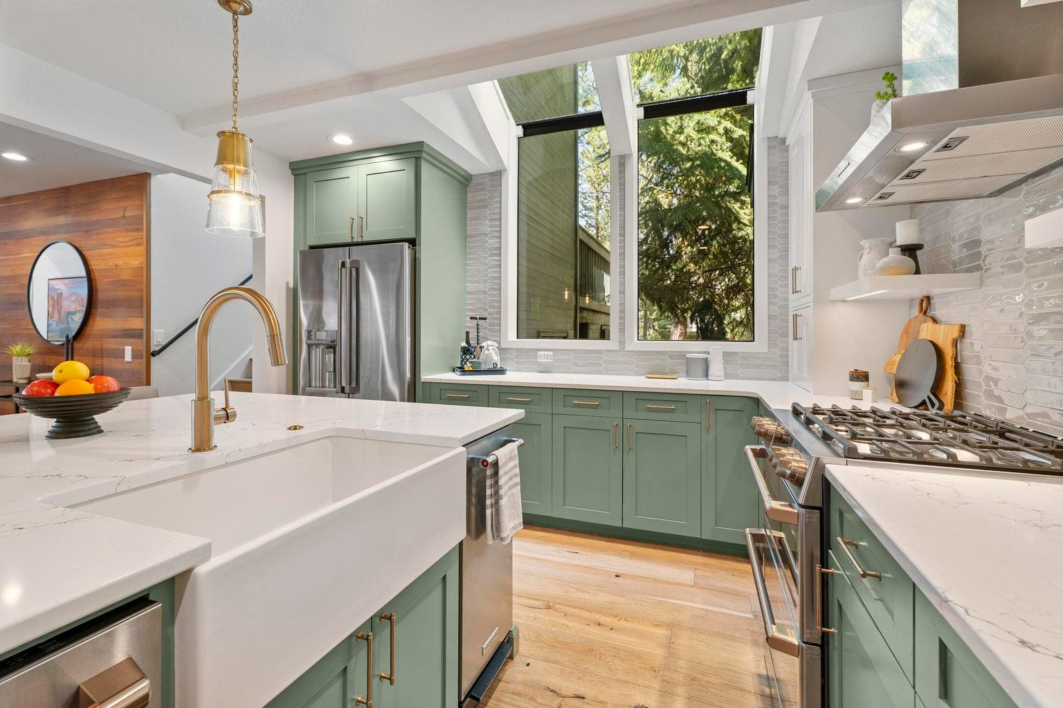 Stylish, with sage green cabinets, white upper cabinetry, gold accents and a large island beneath elegant pendant lighting.
