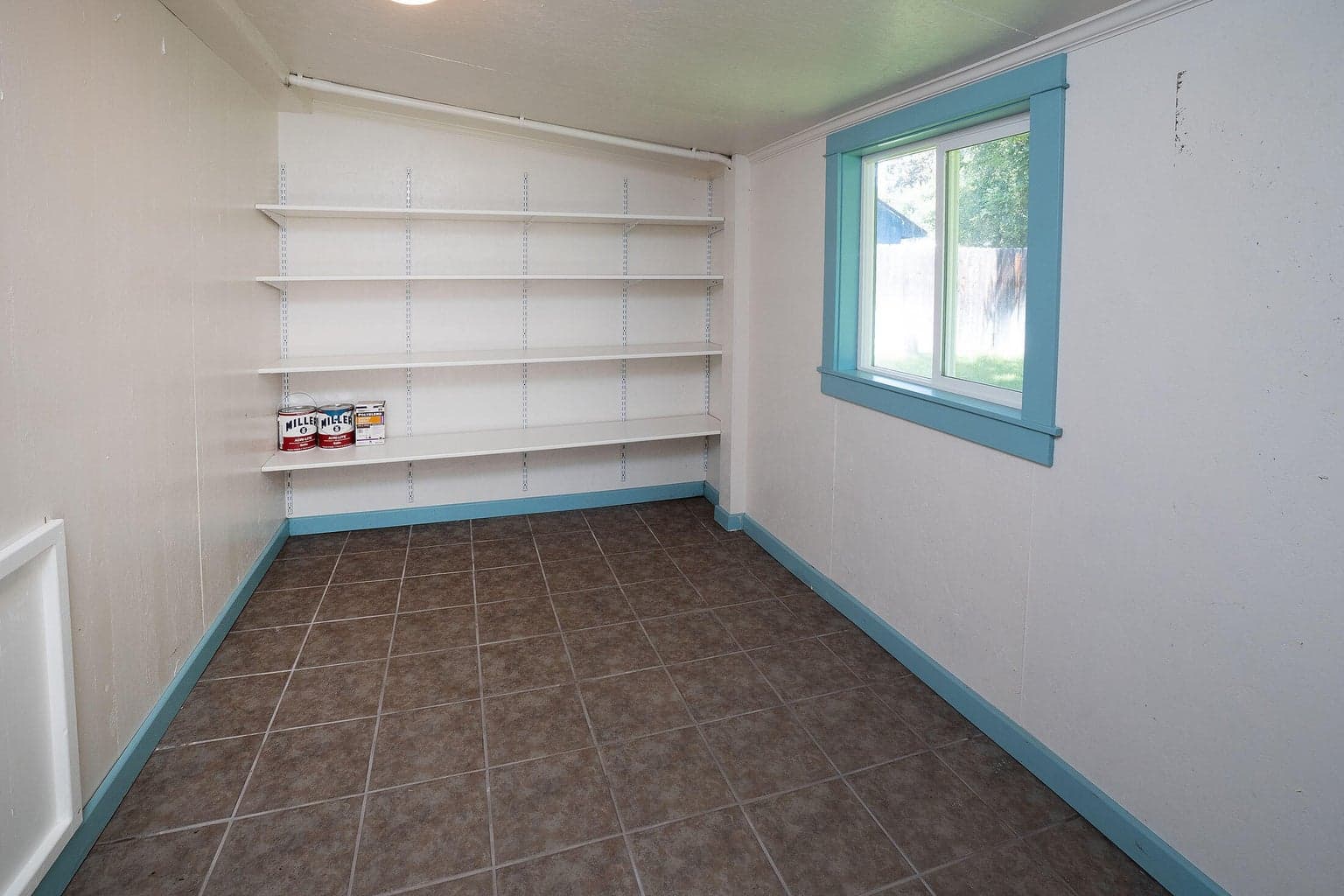 Attached storage room features window, tile flooring, and convenient shelves, and secure entry door.