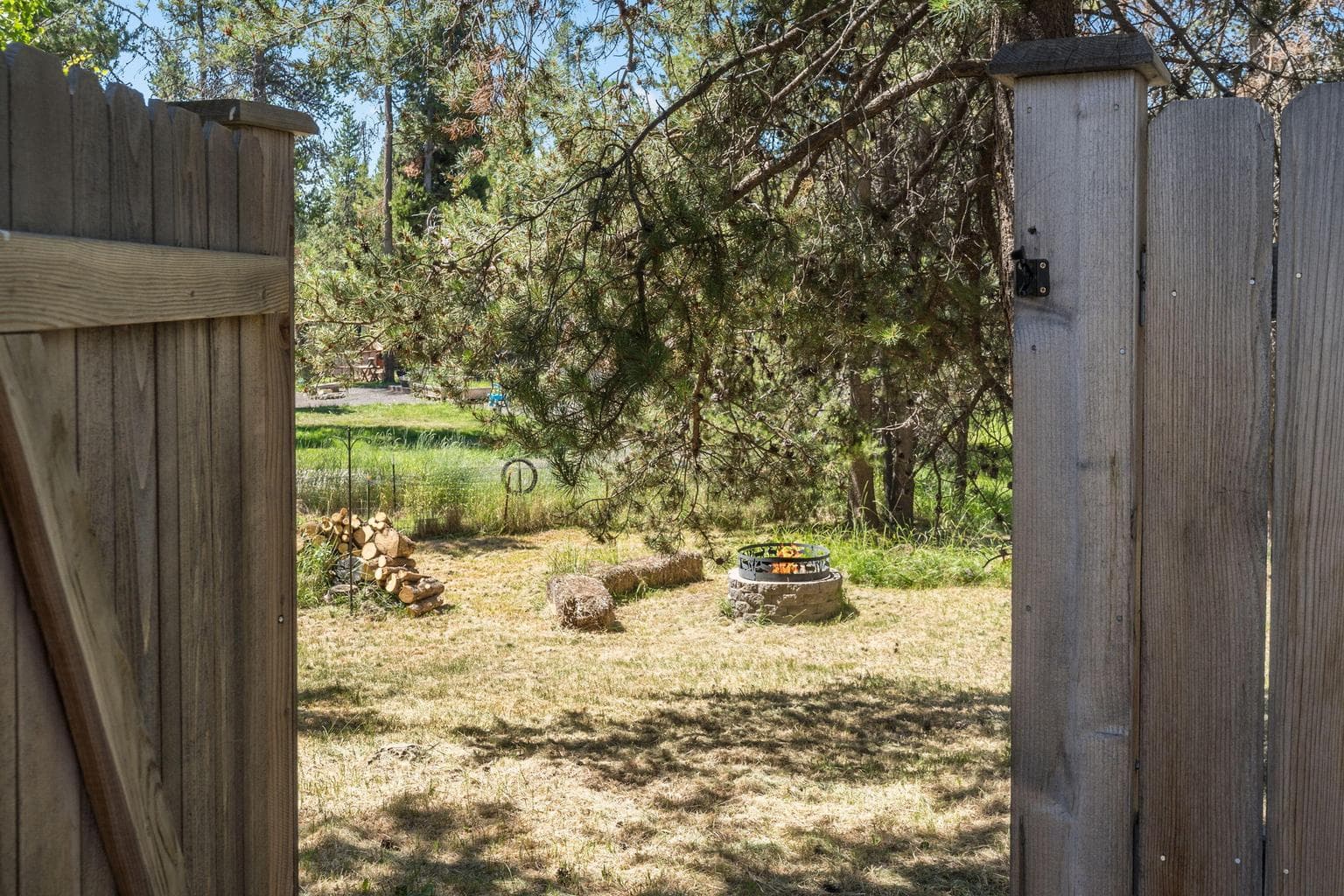 Property extends past fenced in area to wooded area with fire pit.