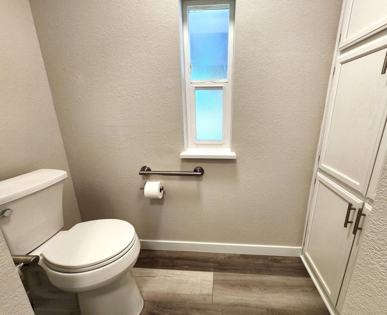 Primary bathroom toilet, grab bar, and linen storage area