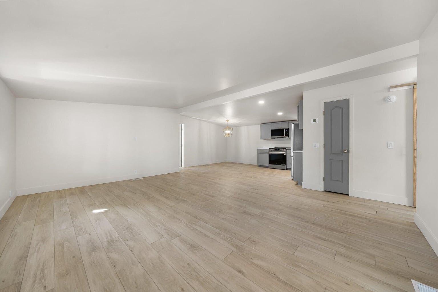 Living room is spacious, has all new LVP flooring, hand textured walls, high ceilings, custom doors, and warm lighting .