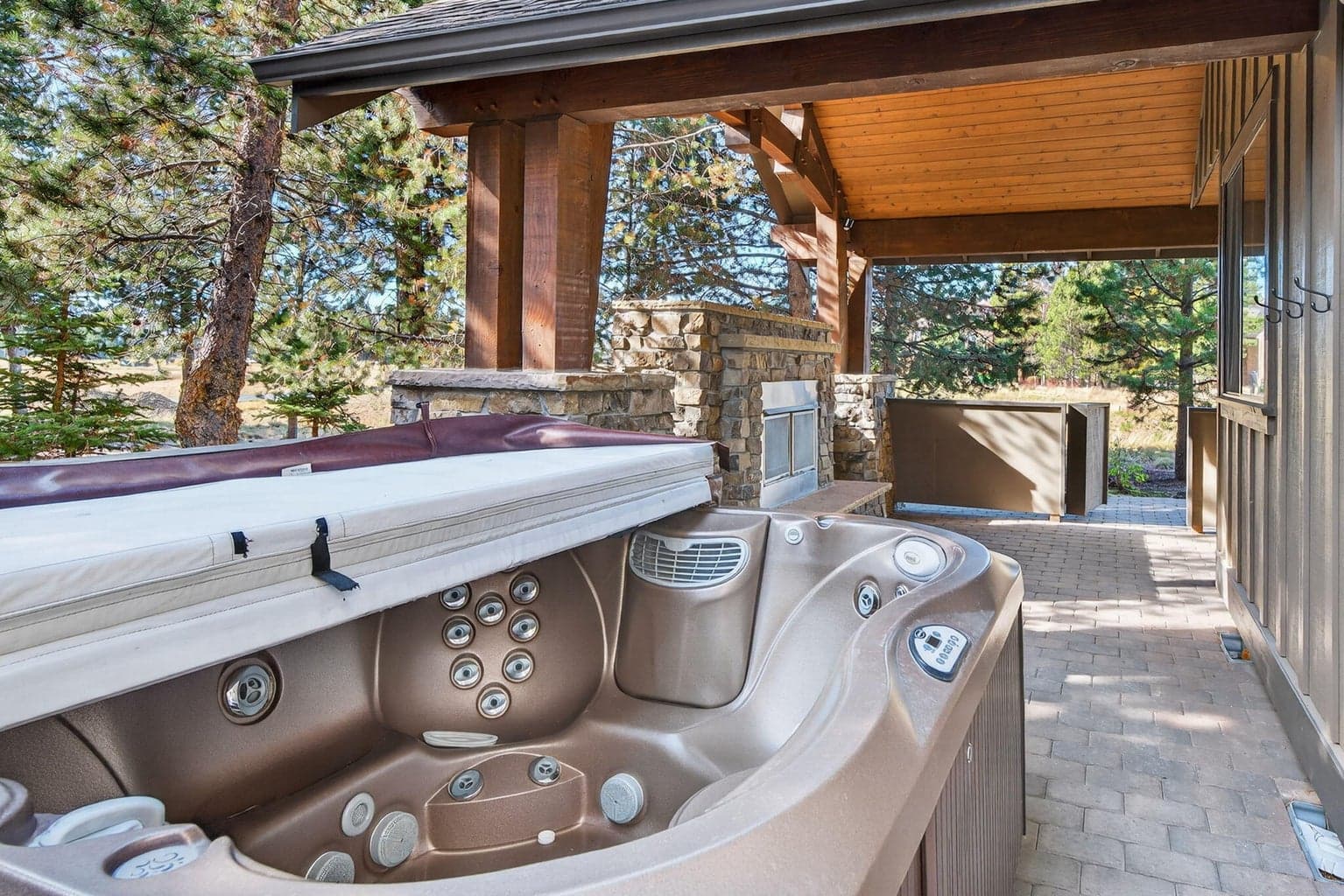 Unwind in your private outdoor retreat featuring a covered patio with a soothing hot tub and double-sided stone fireplace. Sheltered for year-round enjoyment, this inviting space is ideal for evening gatherings, quiet reflection, or a relaxing soak beneath the pines.