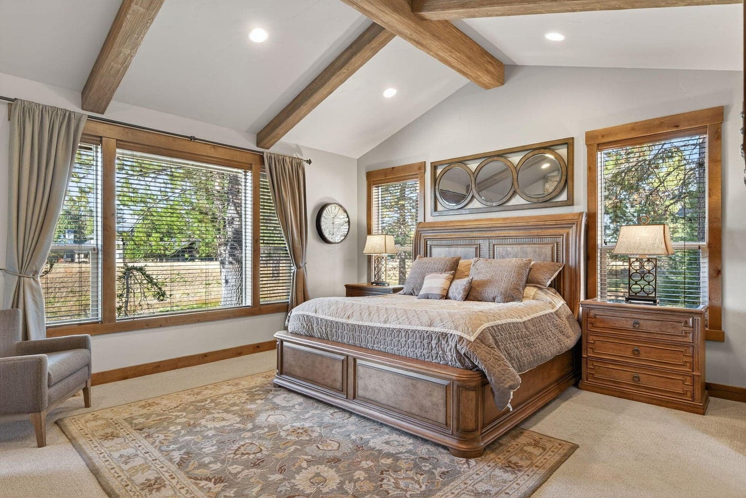 Elegant primary suite featuring a warm fireplace, soaring vaulted ceilings, and expansive windows that fill the room with natural light and serene forest views.