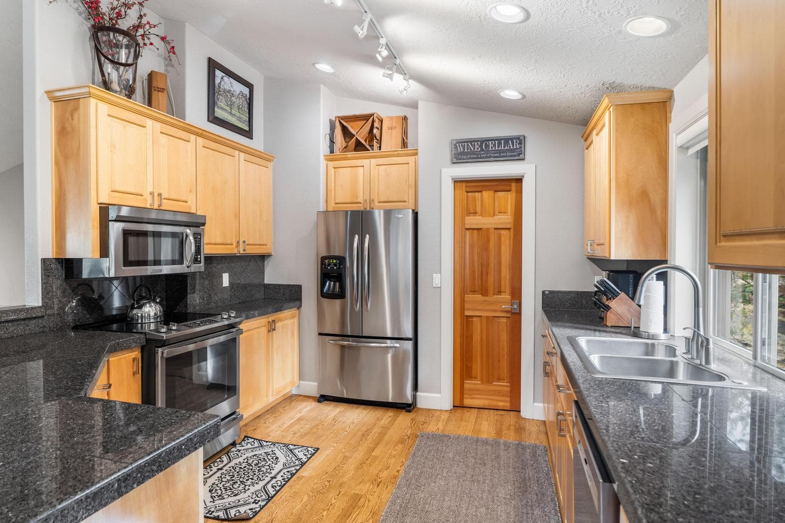 This well-appointed kitchen features granite countertops, stainless steel appliances, and warm natural wood cabinetry. A large window above the sink fills the space with light, while ample counter space and storage make it ideal for cooking and entertaining.