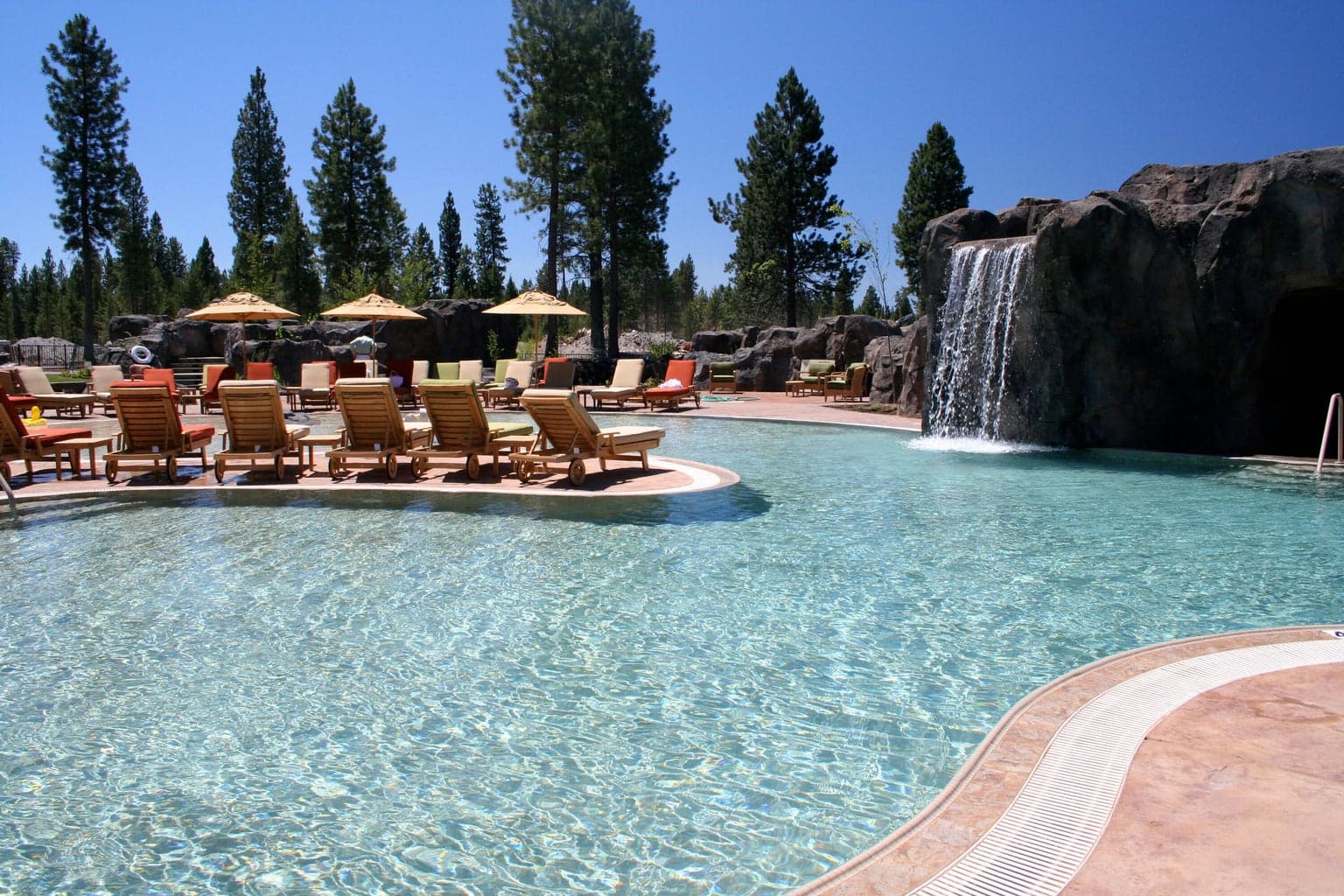 Faux boulders reinforce the illusion that the pool and lake are a single body of water, and also form “grotto” areas for hot tubs. “Lava tube” tunnels and a slide with waterfall provide enjoyable areas for children to explore in a lively family atmosphere.