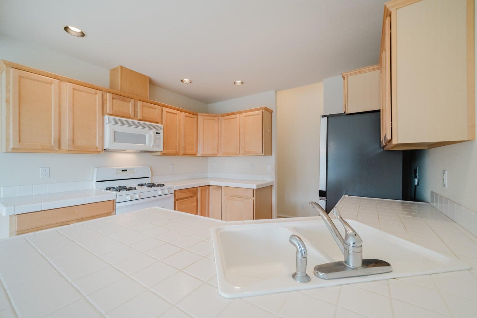 Tiled countertops, gas stove/range with a microwave hood vent, dishwasher and stainless steel refrigerator.