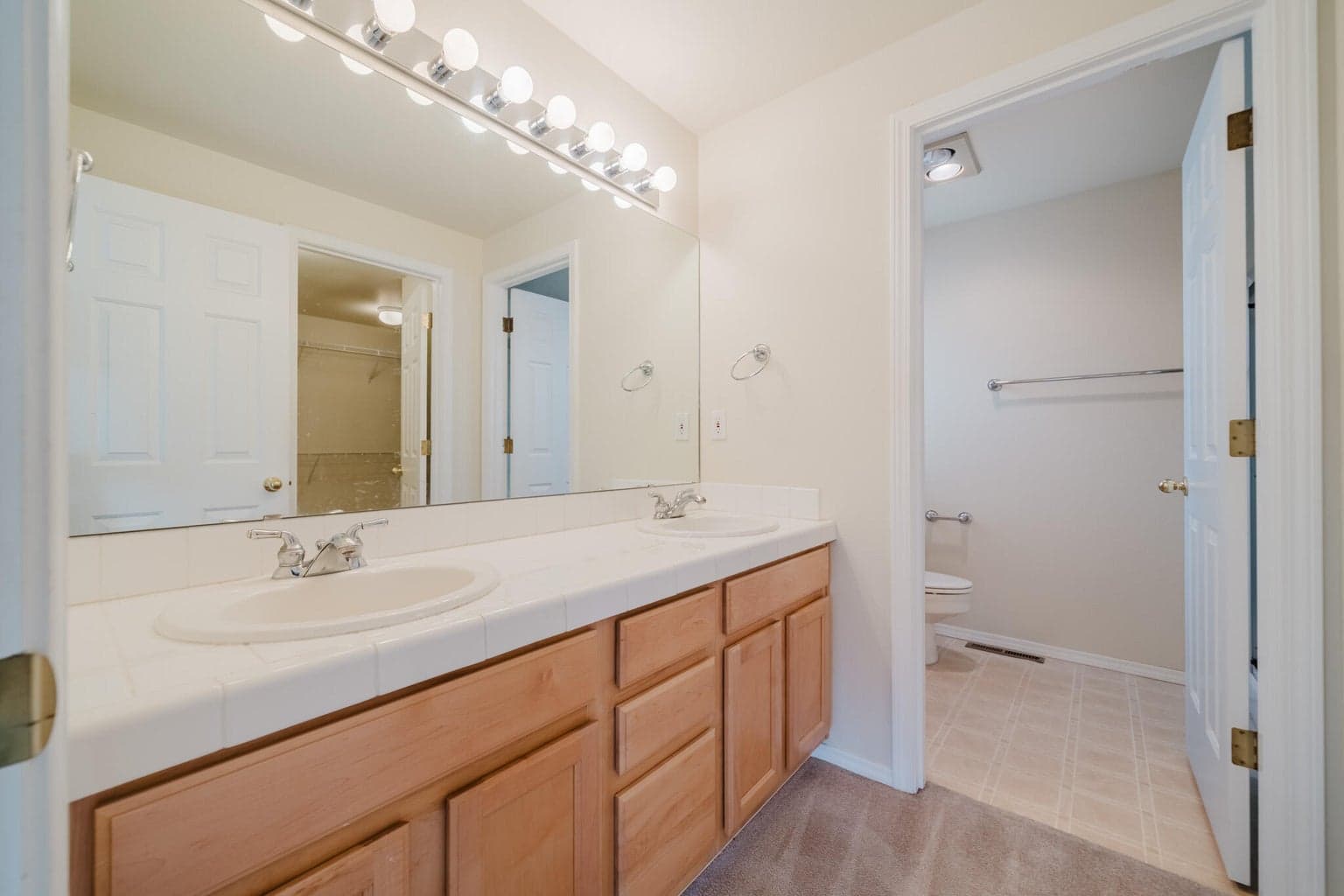 Dual vanity with tiled countertop, full length mirror and a long run of globe lights. Separate room has the shower and toilet.