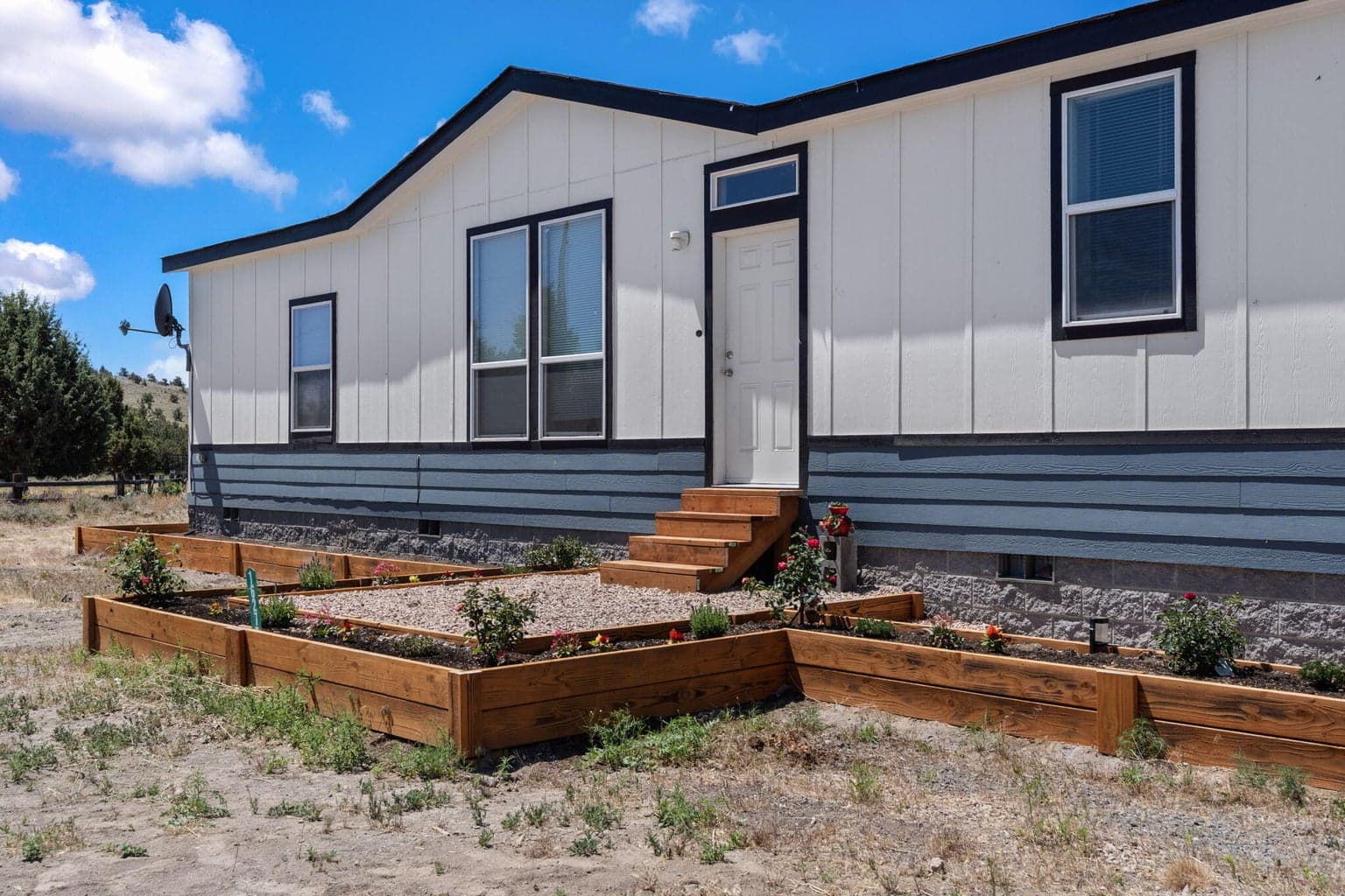 Framed by a long gravel driveway and includes tiered wooden garden beds at the entry.