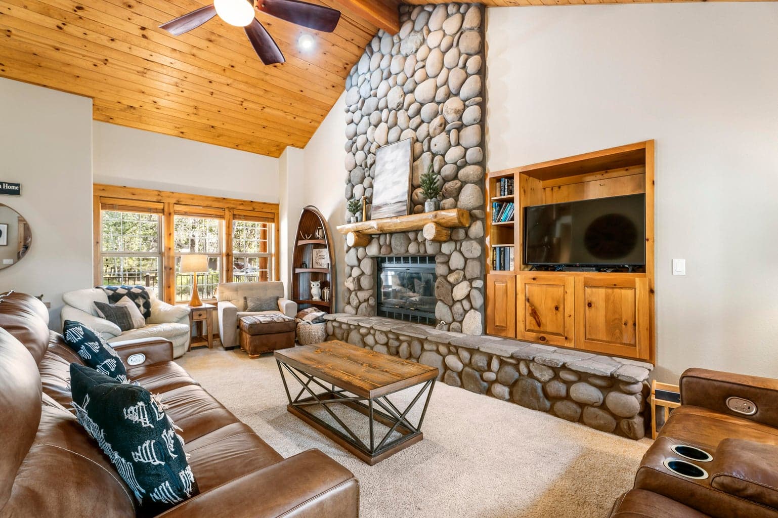 This cozy living room features a stunning floor-to-ceiling river rock fireplace, warm wood accents, and comfortable seating that creates a perfect mountain retreat ambiance.