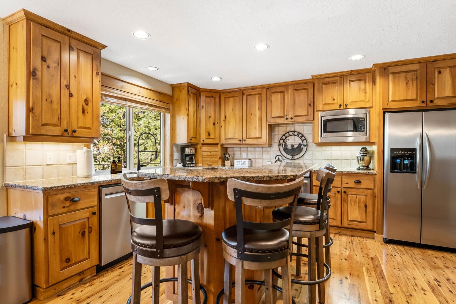 This inviting kitchen showcases natural wood cabinetry, granite countertops, and stainless steel appliances, all beautifully framed by a large window.