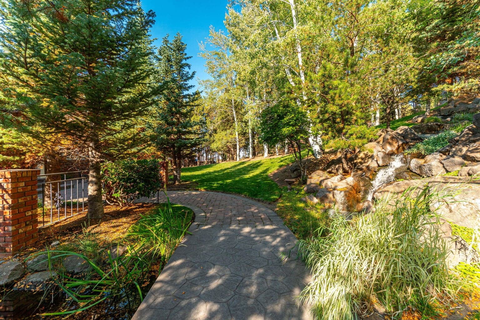 A storybook path winds through lush greenery, past a babbling waterfall, leading to the welcoming courtyard and grand double-door entry.