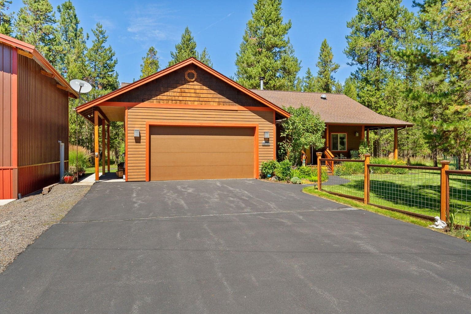 Large, asphalted, front driveway lined with wildflowers and an accent fence.