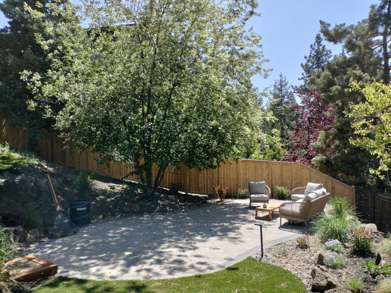 Professionally landscaped grounds surround the paver patio, where blooming trees and established shrubs enhance privacy and natural beauty.