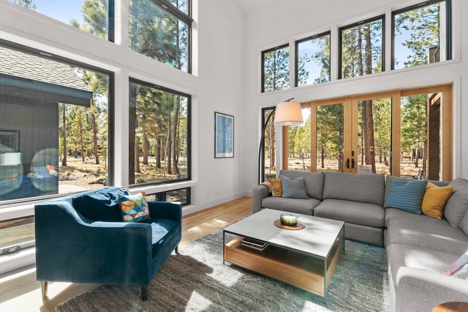Dramatic, light-filled great room with soaring vaulted ceilings, walls of glass, and a striking floor-to-ceiling poured concrete fireplace surround. Exposed wood accents, clean contemporary lines, and warm natural textures create a true mountain modern centerpiece.