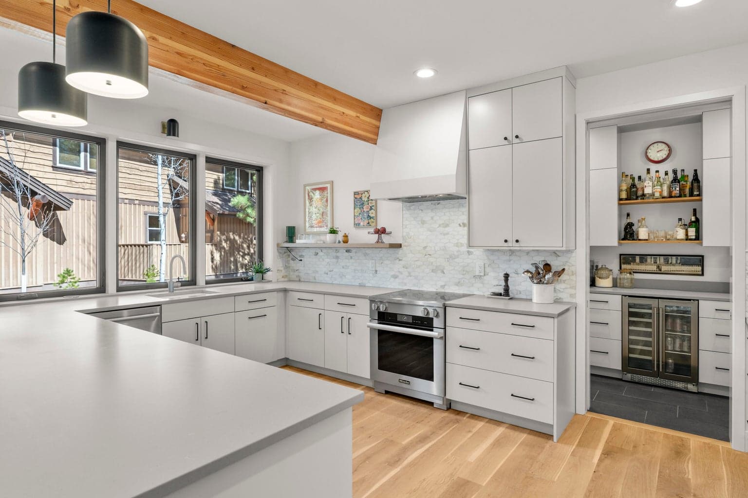 Thoughtfully designed for everyday living and entertaining, the kitchen offers a large work island, extensive drawer storage, contemporary pendant lighting, and clean architectural lines. The bright white palette is balanced by warm wood flooring and exposed beam detail for a refined, inviting look.