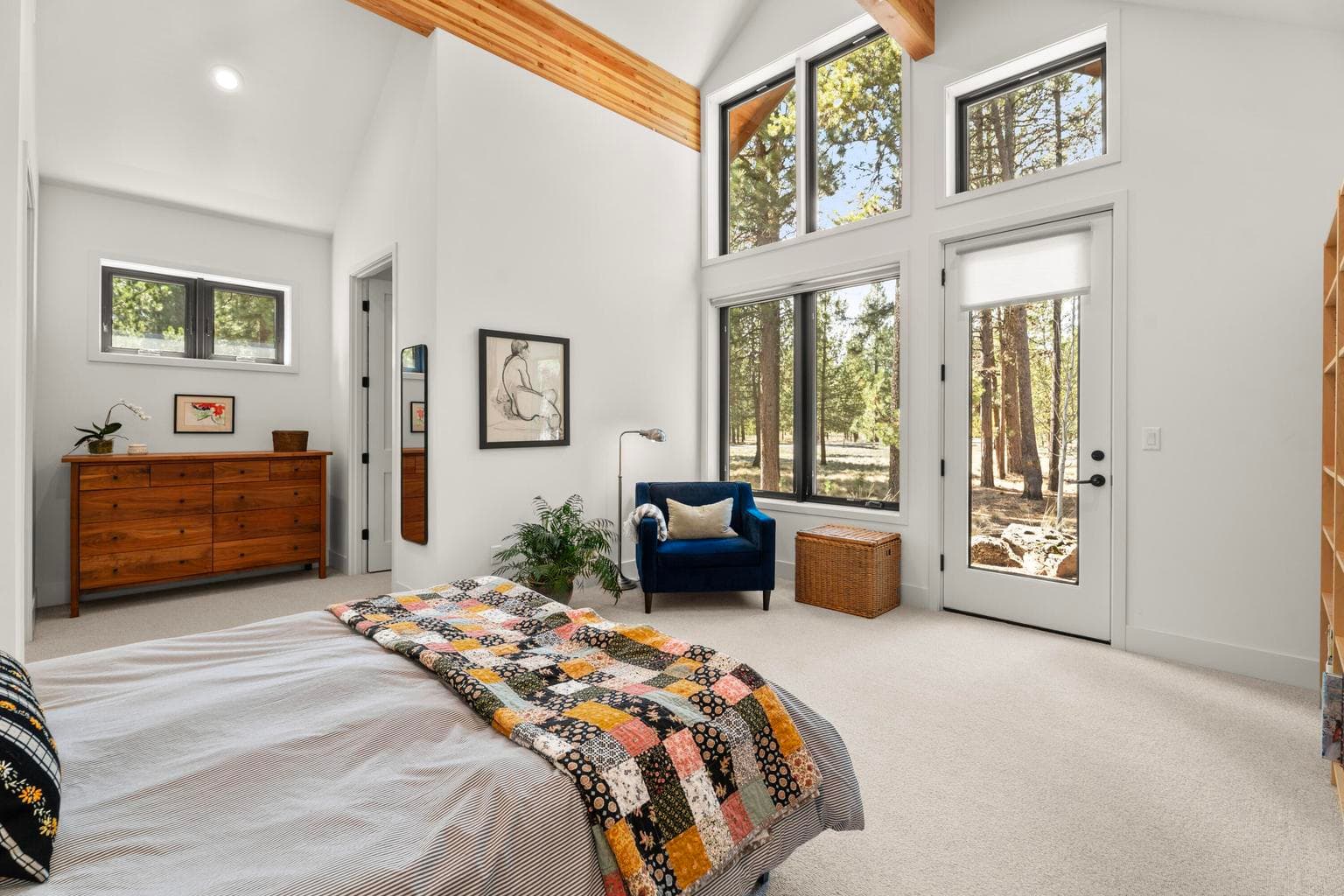 A beautifully scaled primary suite with vaulted ceilings, warm beam accents, and expansive windows that bring in abundant natural light and treed outlooks. The room feels open, restful, and distinctly connected to its natural setting.