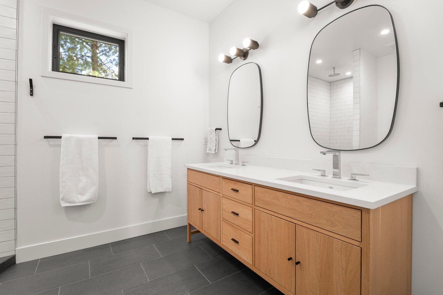 The primary bath blends warmth and simplicity with a double vanity, quartz-style counters, modern lighting, and natural wood cabinetry. The large walk-in shower with full-height tile and built-in bench creates a bright, polished retreat.