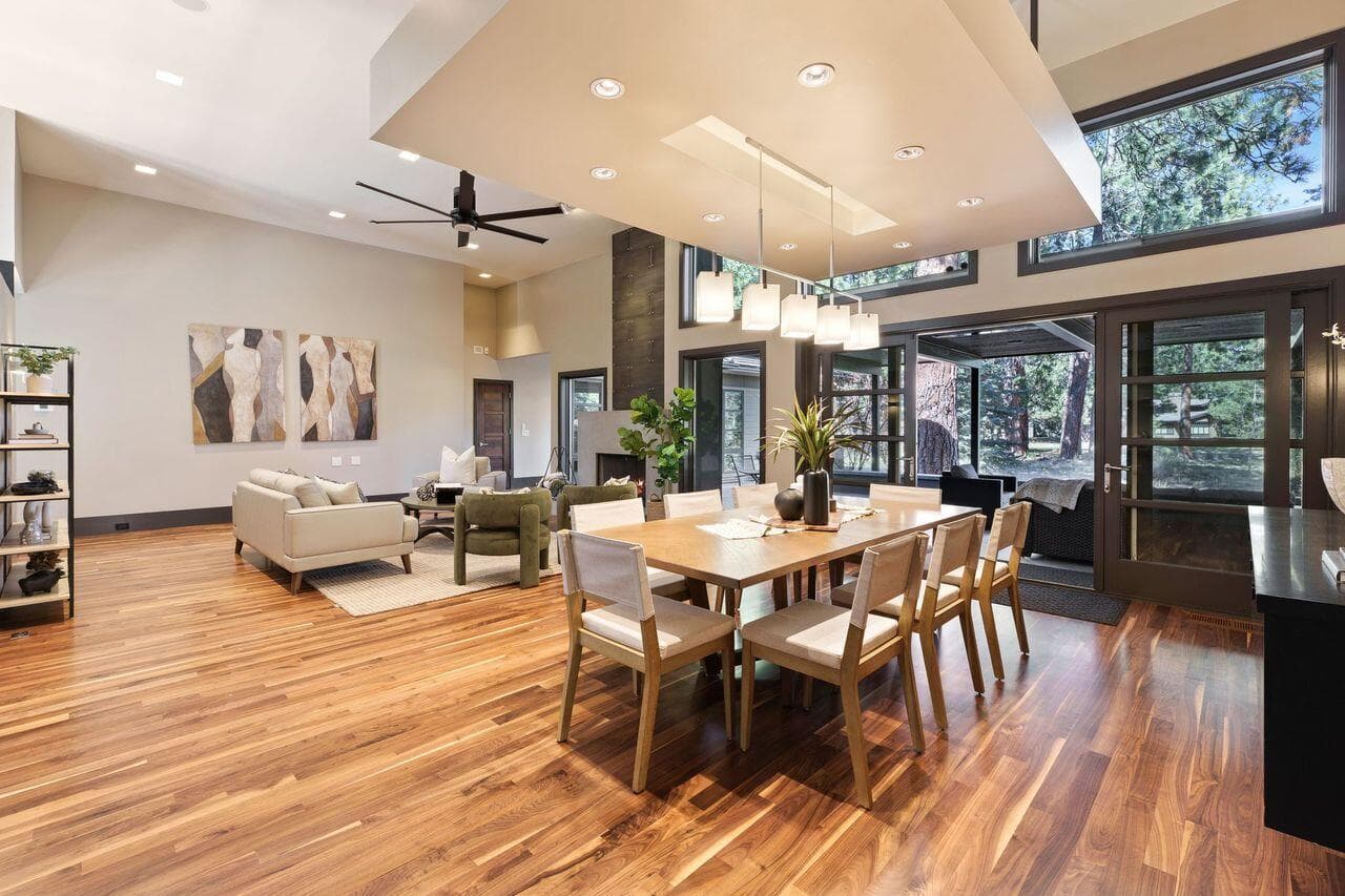 Open-concept living and dining space with seamless indoor-outdoor flow, highlighted by expansive windows, warm walnut flooring, and clean modern lines throughout.