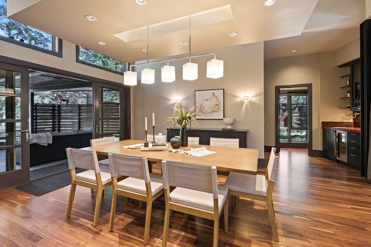 Dining area with custom lighting, warm walnut flooring, and seamless access to the covered outdoor living space.