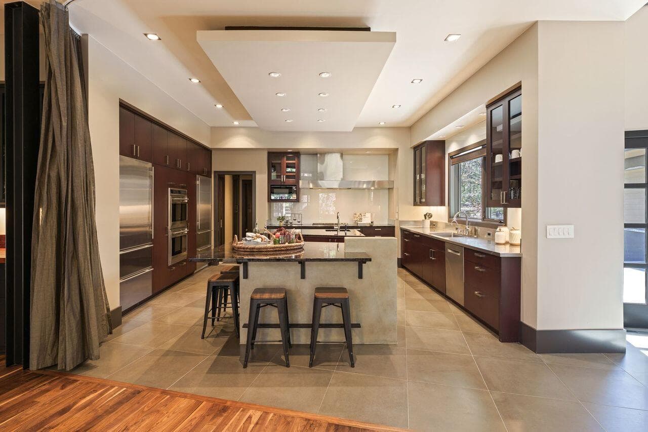 Kitchen featuring custom cabinetry, stone countertops, and a central island with seating, thoughtfully designed with exceptional functional flow for both everyday use and gathering. A full-height integrated curtain provides the option to separate the kitchen from the dining area, offering flexibility for entertaining while maintaining the home’s clean architectural lines.