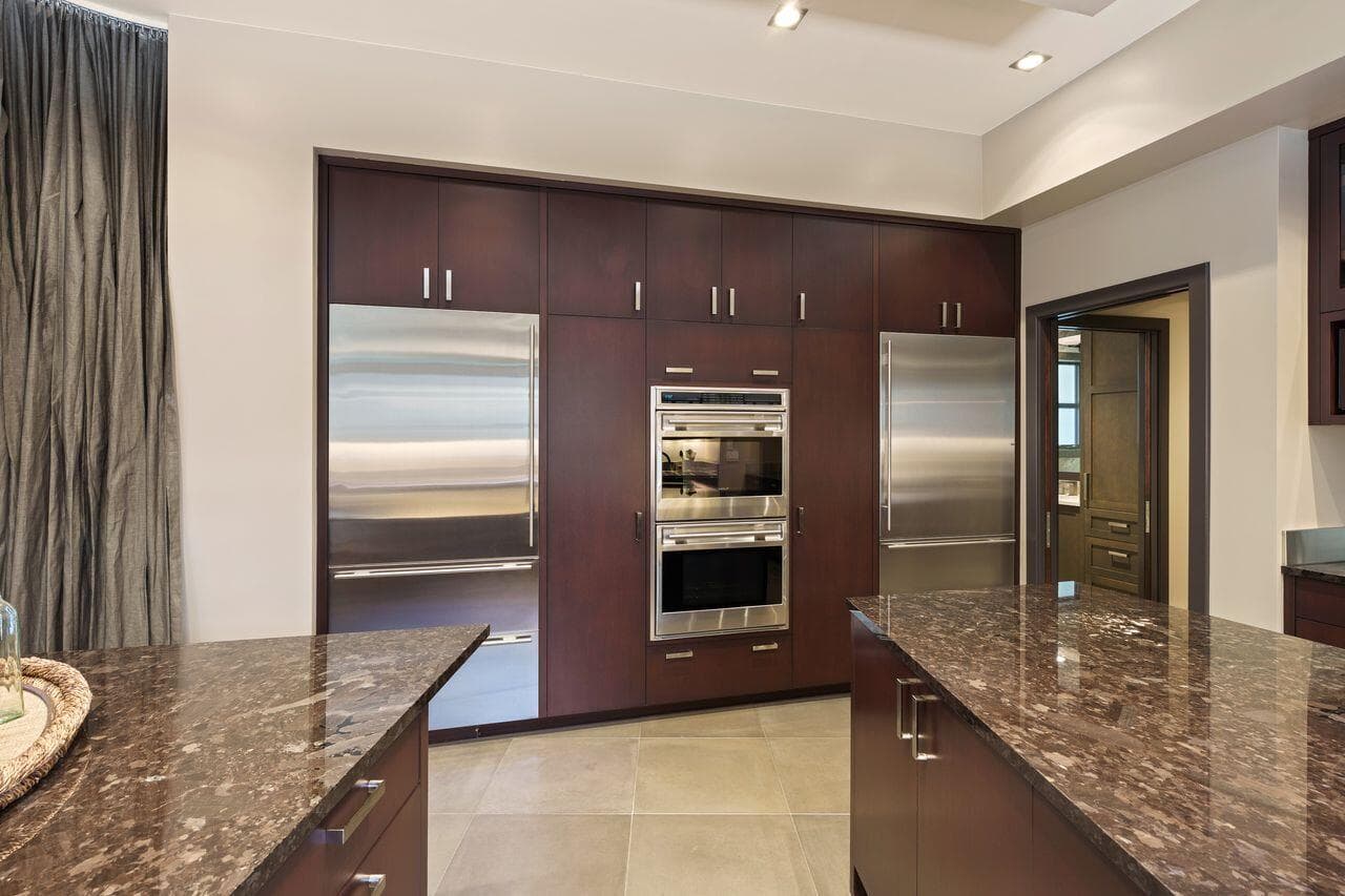 Kitchen featuring custom cabinetry, stone countertops, and integrated appliances, including Wolf double wall ovens, a Sub-Zero refrigerator, and a concealed reach-in pantry seamlessly integrated behind matching panels on the left—designed for both function and efficiency.