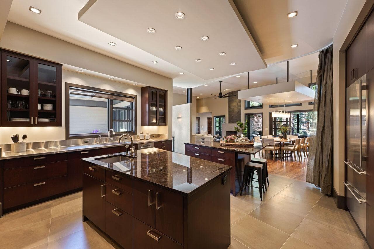 Kitchen featuring dual trapezoidal islands with stone countertops and custom cabinetry, thoughtfully designed with exceptional functional flow. The layout opens seamlessly to the dining and living areas, supporting both everyday living and easy entertaining.