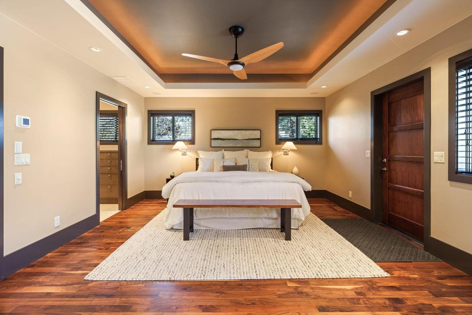Private primary suite with warm wood floors, tray ceiling detail, and direct access to a well-appointed bath and closet spaces.