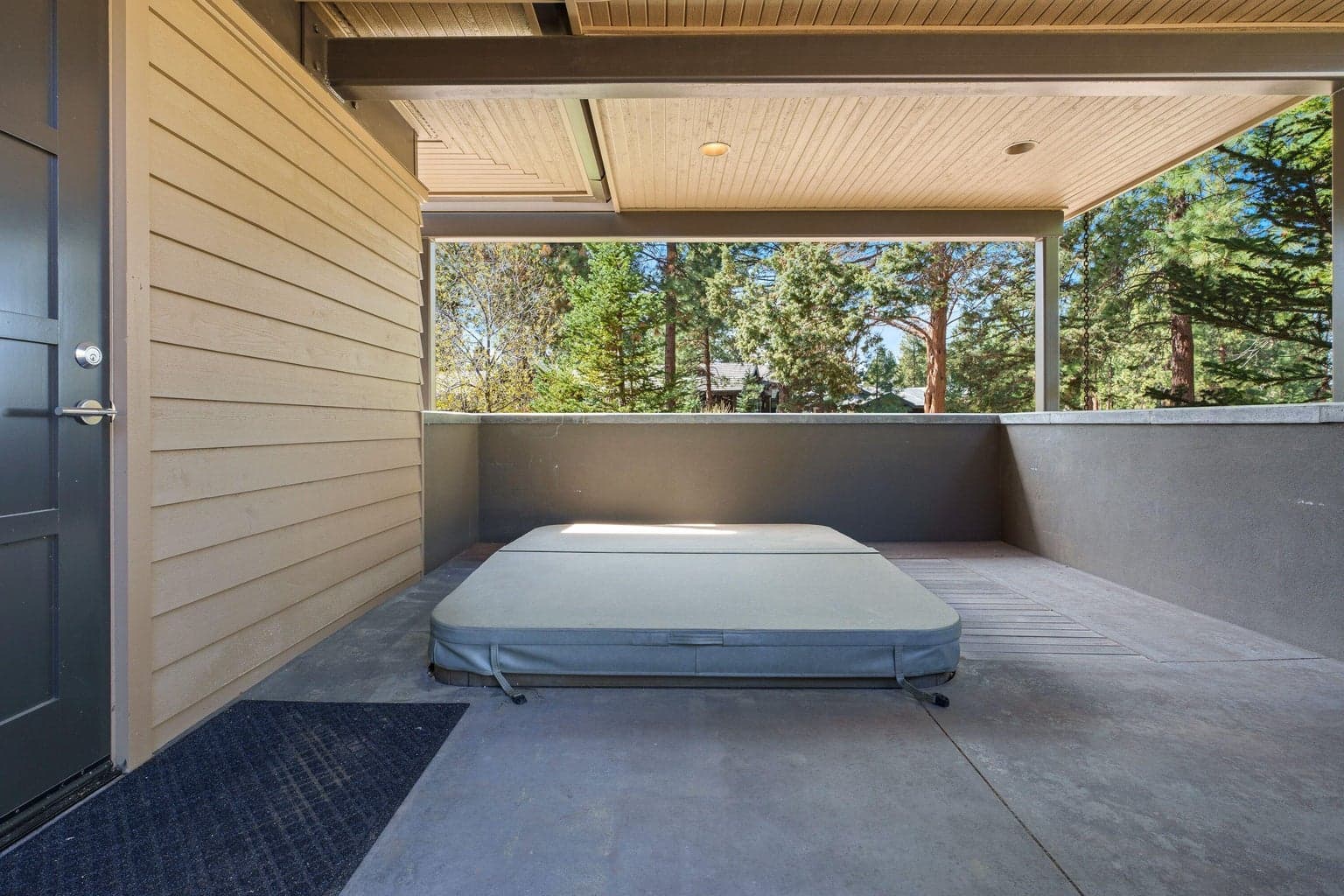 Private covered patio off the primary suite featuring a sunken hot tub—creating a quiet, tucked-away retreat with peaceful treed views.