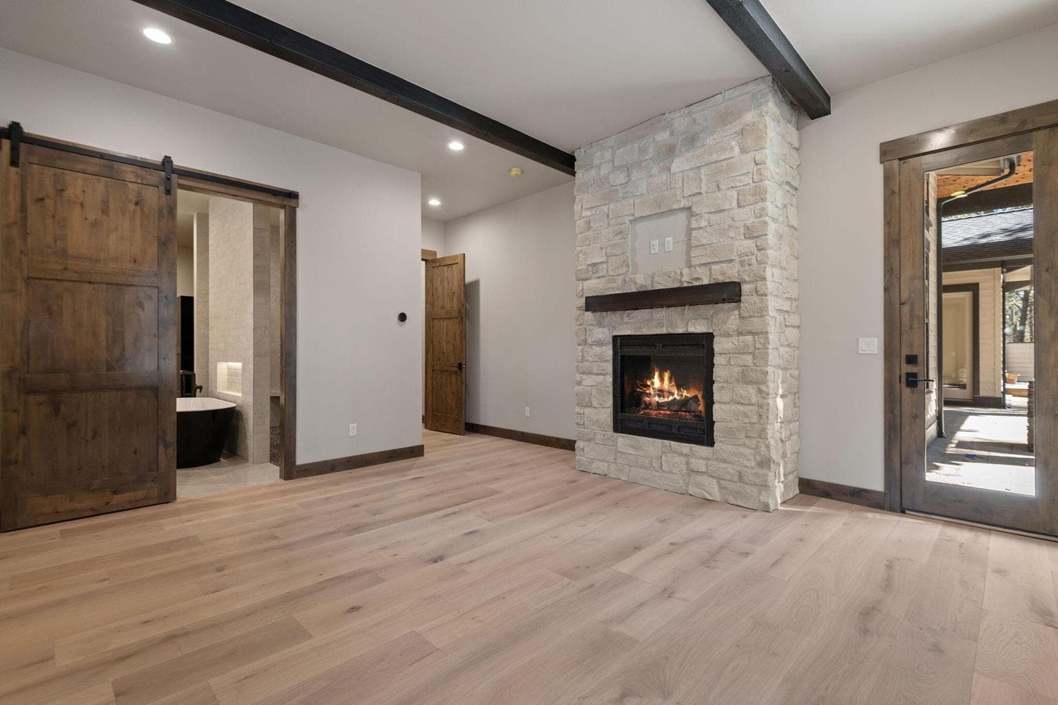 Main level Primary with bath ensuite with custom barn door, custom beamed ceiling, rocked gas fireplace, and entry to exterior and patio