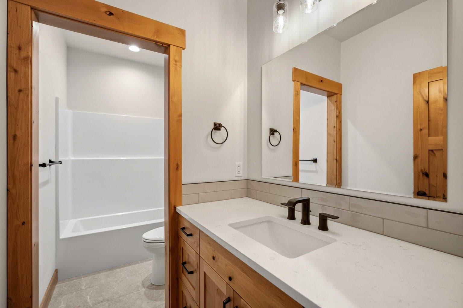 Well-appointed guest bathroom with quartz vanity, warm wood cabinetry, and stylish finishes designed for comfort and convenience.