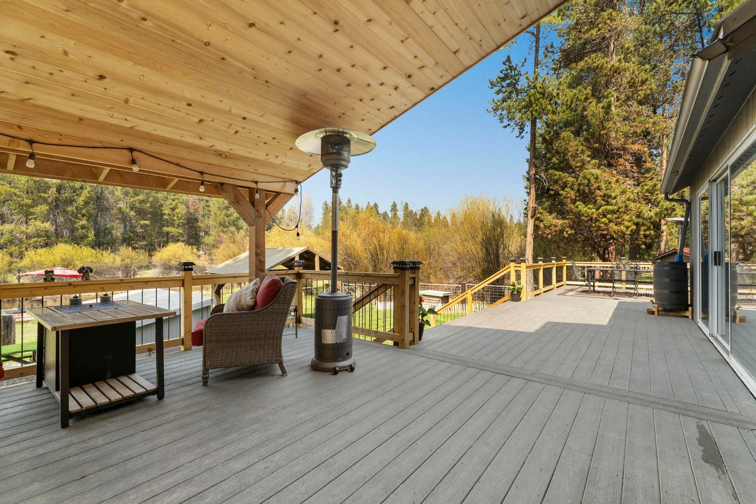 Covered deck with patio heater and string lights framed by towering pines