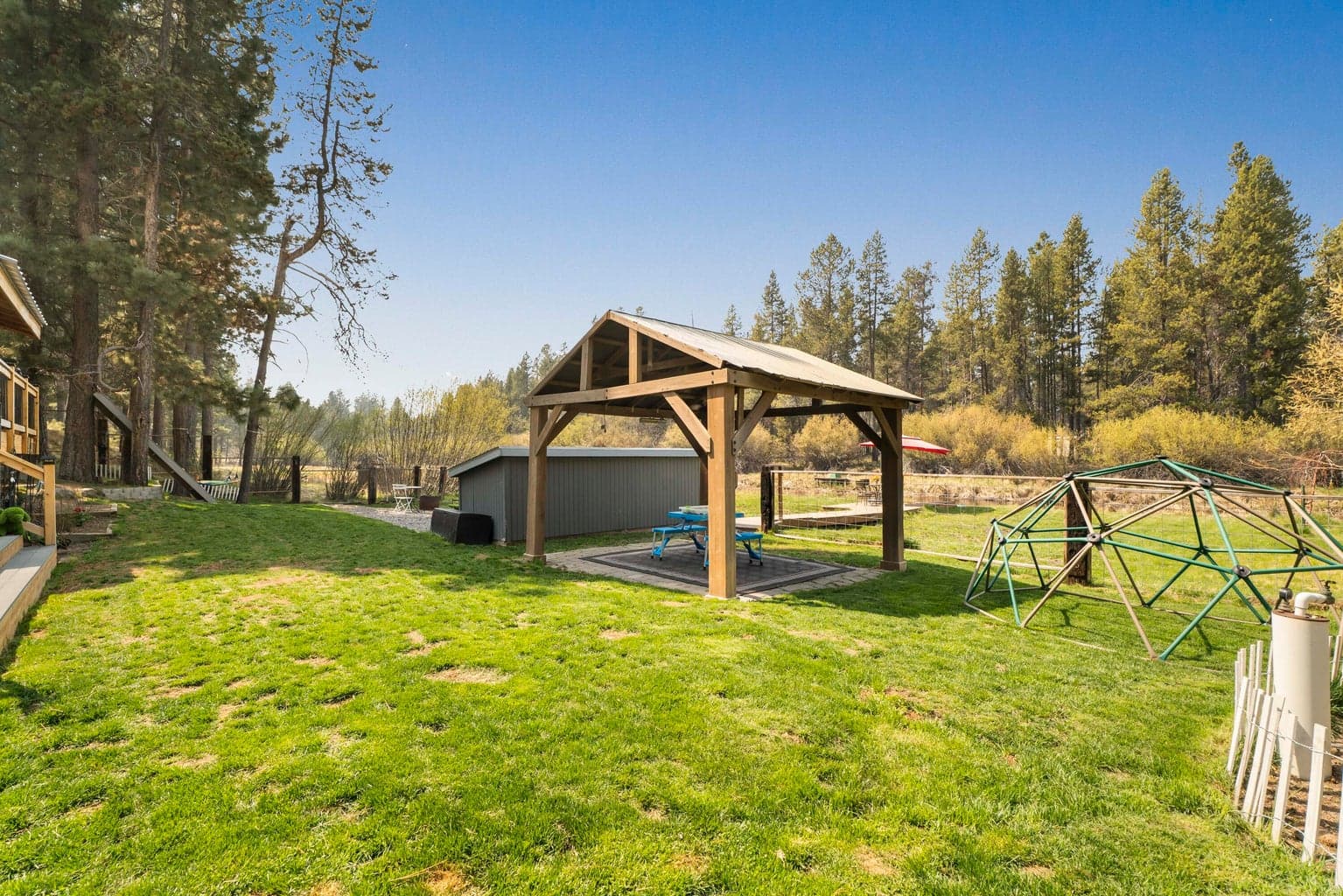 Timber-frame pavilion, climbing dome, and fenced lawn — the family compound