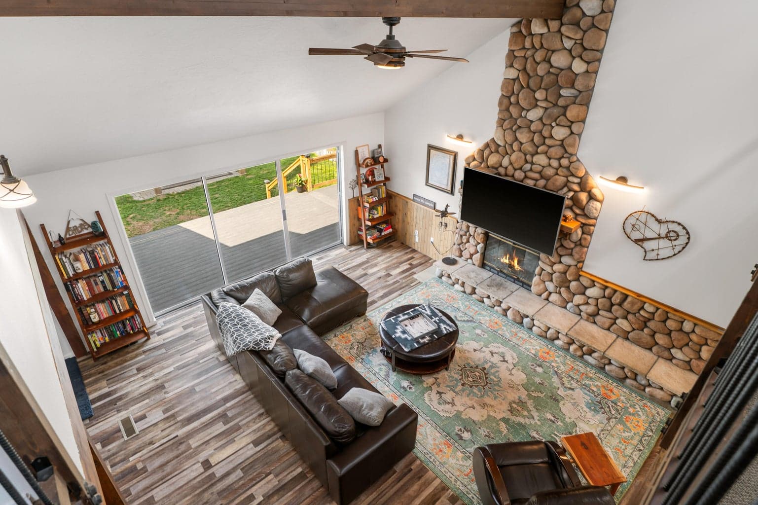 Living room reveal from the loft with vaulted ceilings and floor-to-ceiling river-rock fireplace
