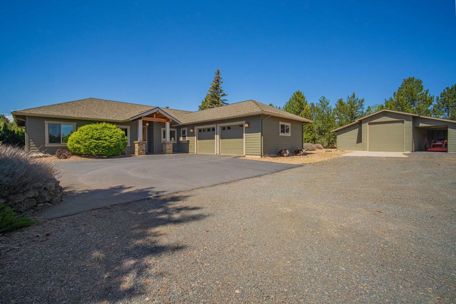 Front exterior view showing the home, detached barn/shop, generous parking, and natural low-maintenance landscape design.