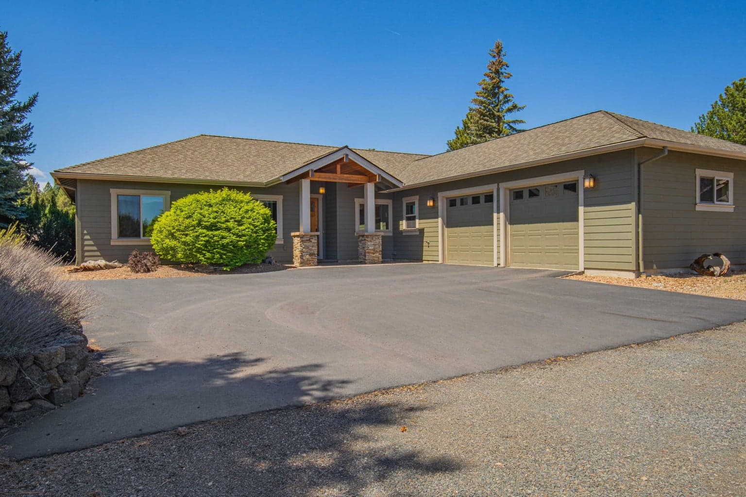 Welcoming front approach with covered entry, attached garage, gravel drive, and a private acreage feel.
