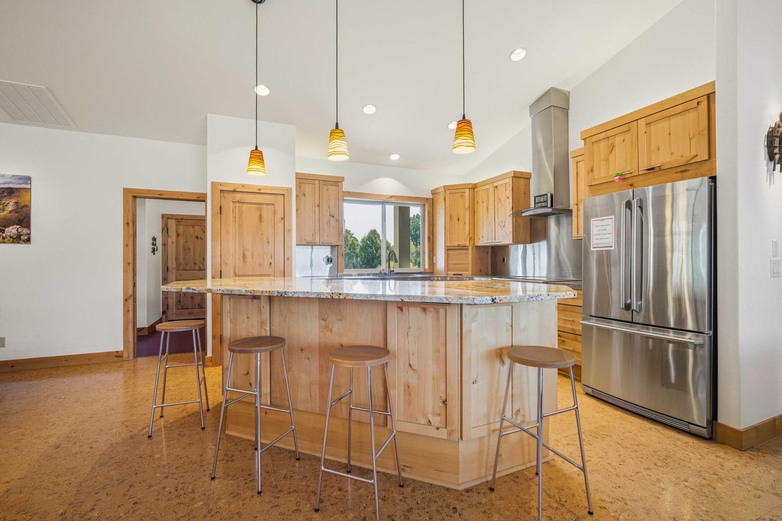 Custom kitchen with large center island, granite surface, pendant lighting, stainless appliances, and warm wood cabinetry.
