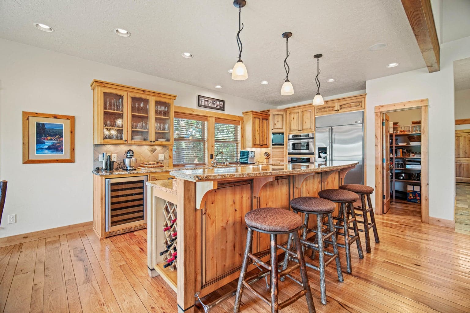 Kitchen with generous island seating, granite counters, warm wood cabinetry, wine storage, and stainless appliances.