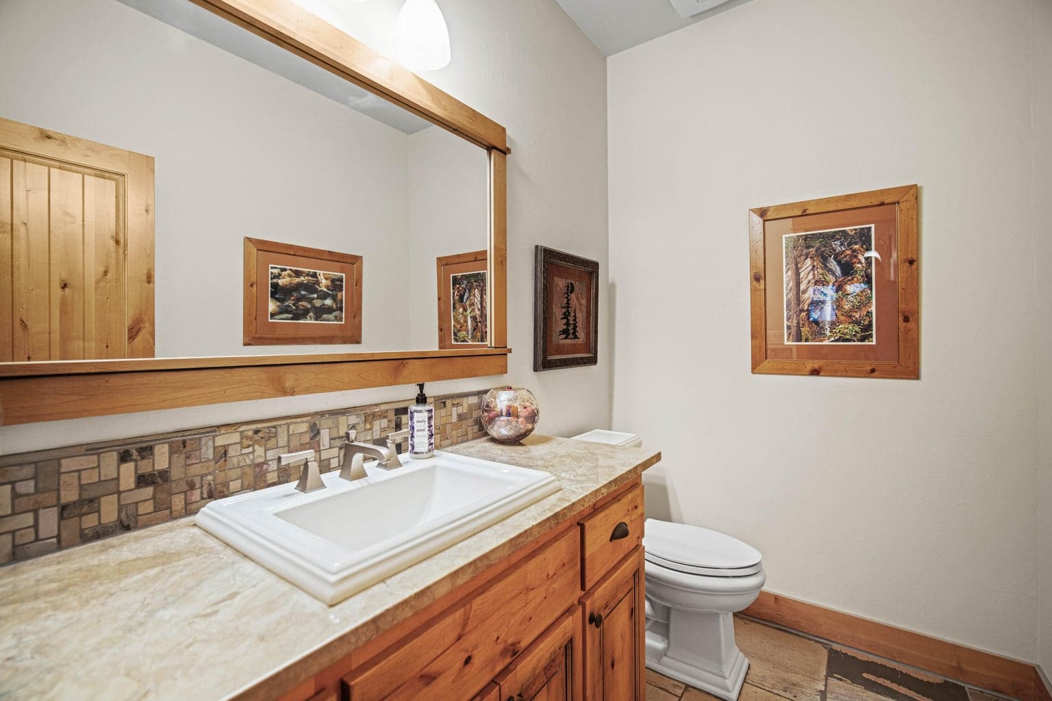 Main-level powder bath with granite counter, wood vanity, framed mirror, and warm Caldera Springs finishes.
