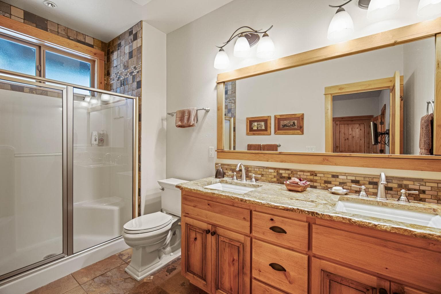 Guest suite bath with dual-sink vanity, granite counter, wood cabinetry, tile accents, and glass-enclosed shower.
