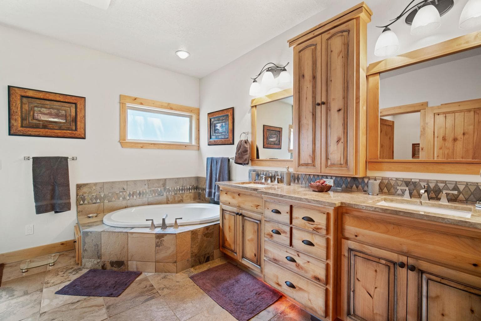 Spacious primary bath with dual vanities, soaking tub, tile flooring, and warm wood cabinetry.