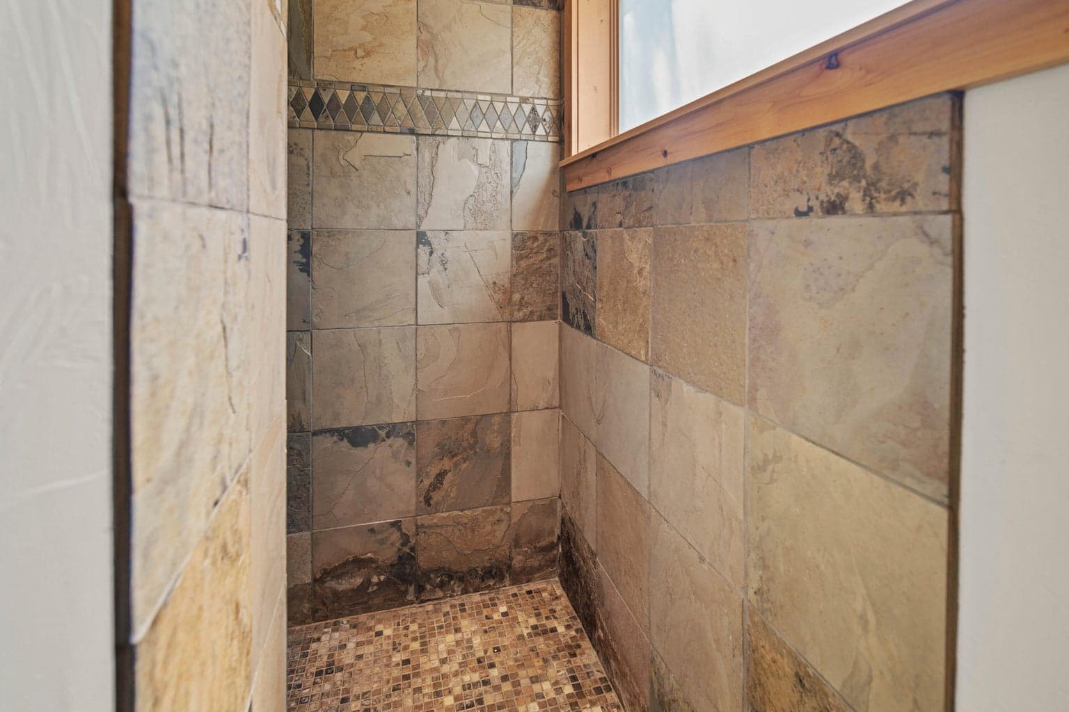 Tile shower detail with natural stone tones and decorative accent band