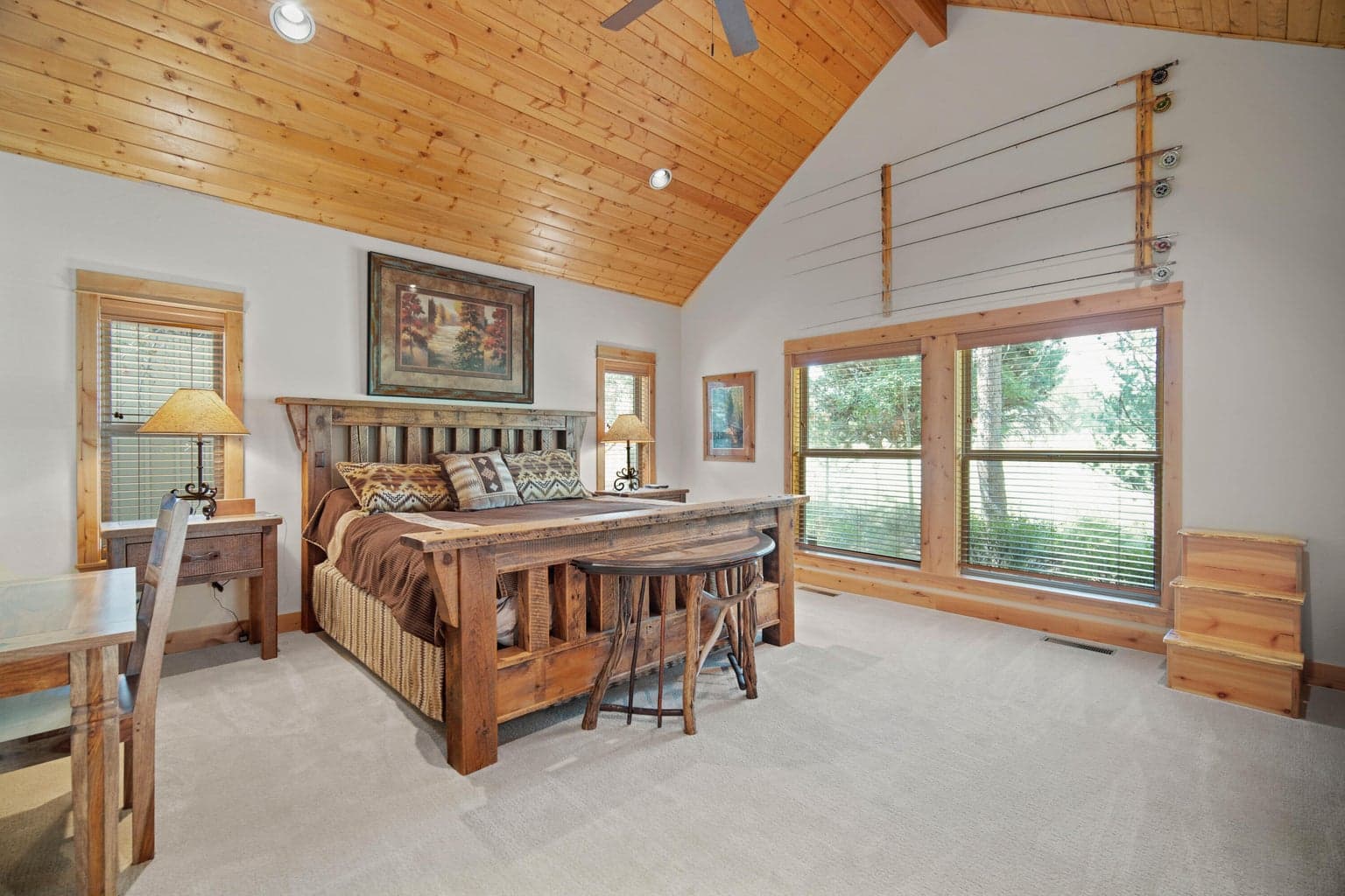 Spacious main-level primary suite positioned on one side of the home, offering a quiet retreat with warm wood trim, large windows, and comfortable separation from the central gathering spaces.