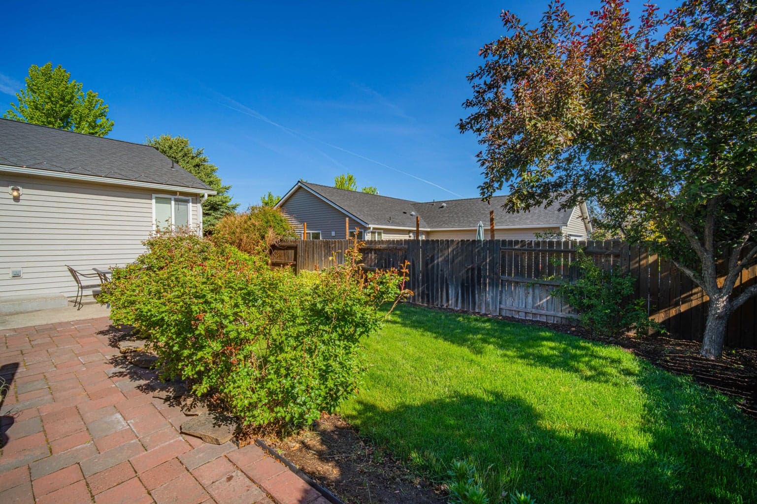 Fully fenced backyard in Bend with a paver patio, lawn area, established landscaping, mature trees, and space for relaxed outdoor living.