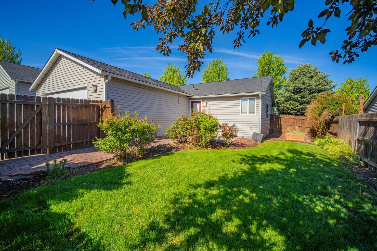 Private backyard setting with a lush lawn, paver patio, mature landscaping, fenced perimeter, and comfortable outdoor space for enjoying Central Oregon sunshine.