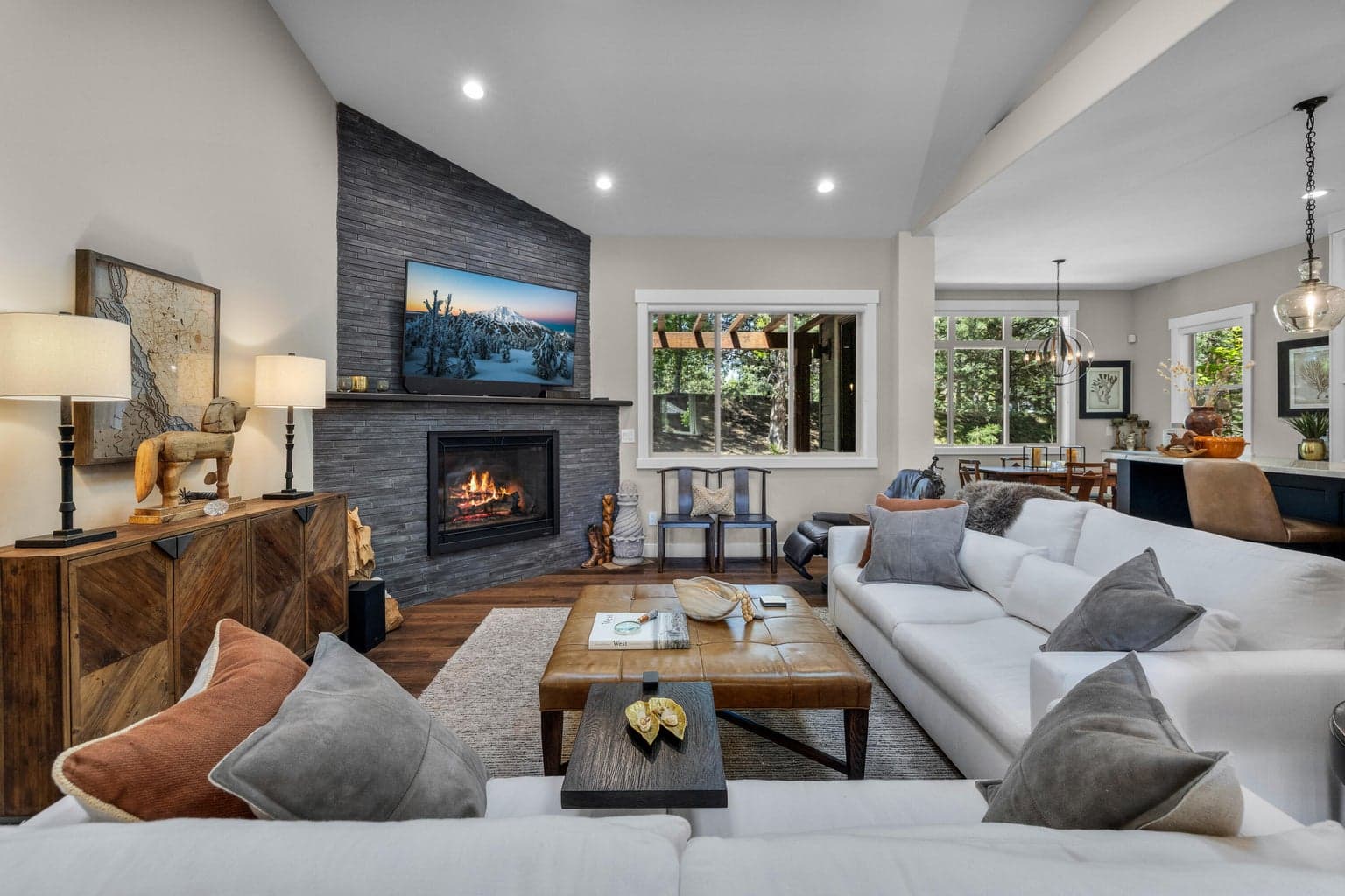 The remodeled great room blends refined comfort with a fresh, open feel, featuring wood floors, a sleek tiled fireplace and generous windows overlooking the outdoor setting.