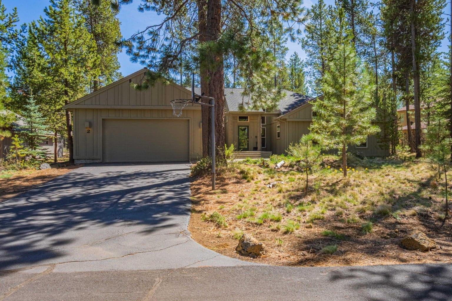 Front exterior of this North Sunriver home, set among native pines with natural landscaping and a paved driveway.