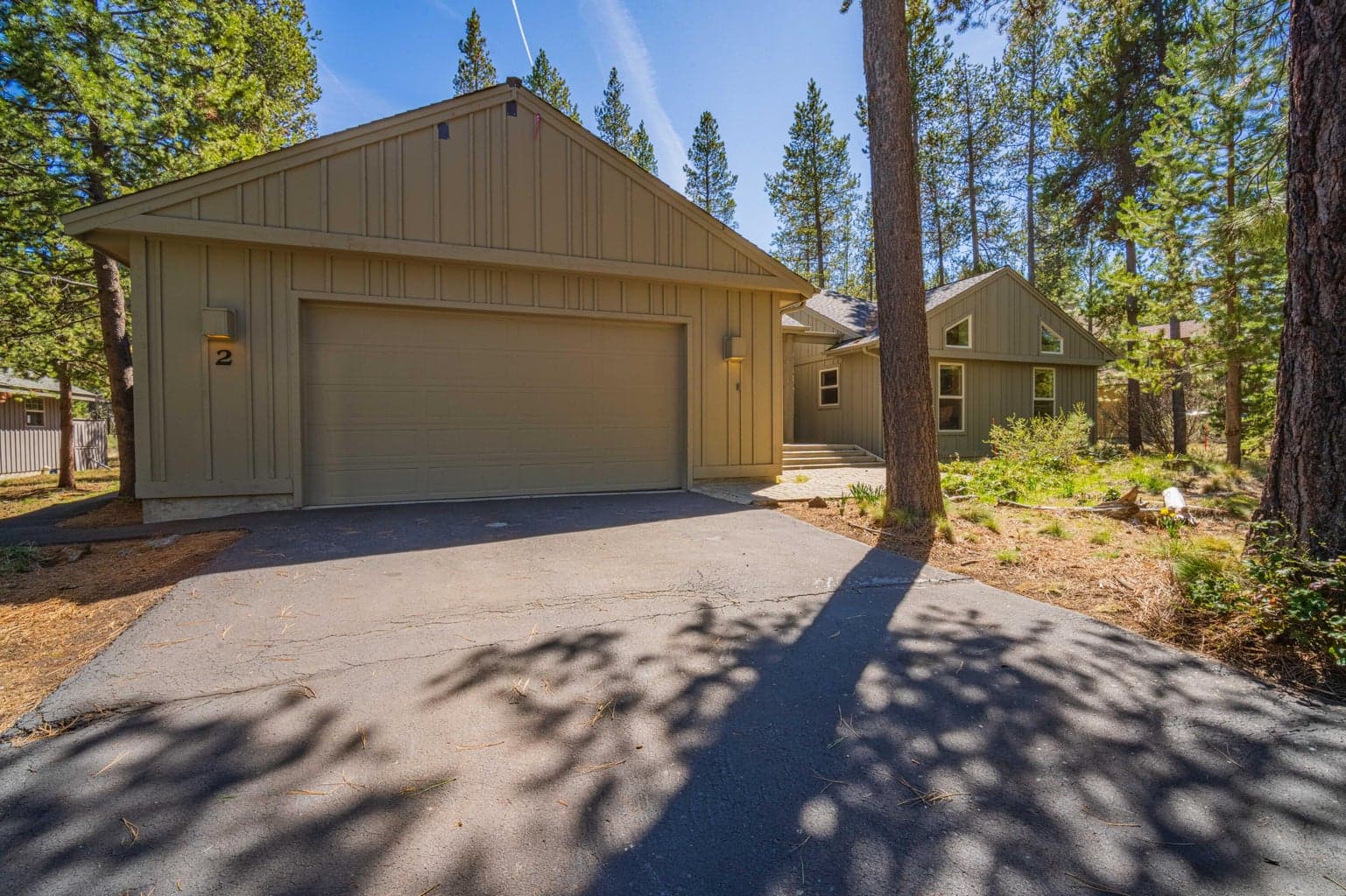 Two-car garage and entry approach at this Sunriver, Oregon home, with mature trees and a quiet north-end neighborhood setting.