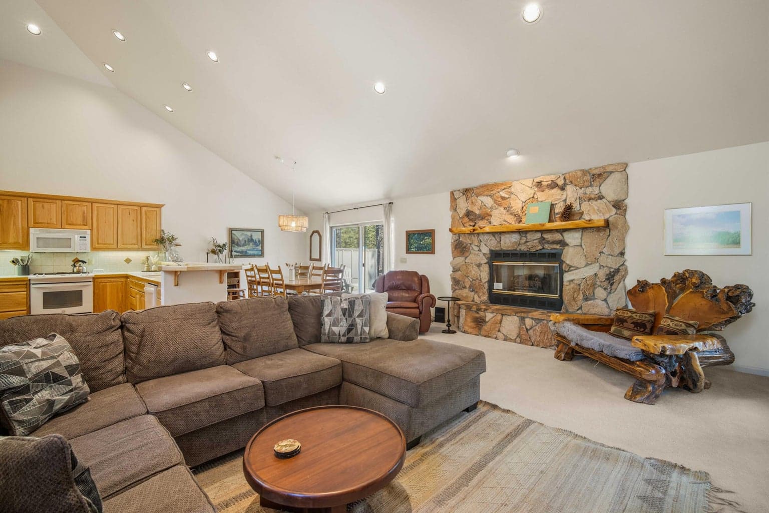 Comfortable Sunriver living room with a large stone fireplace, vaulted ceiling, and easy flow to dining and kitchen spaces.