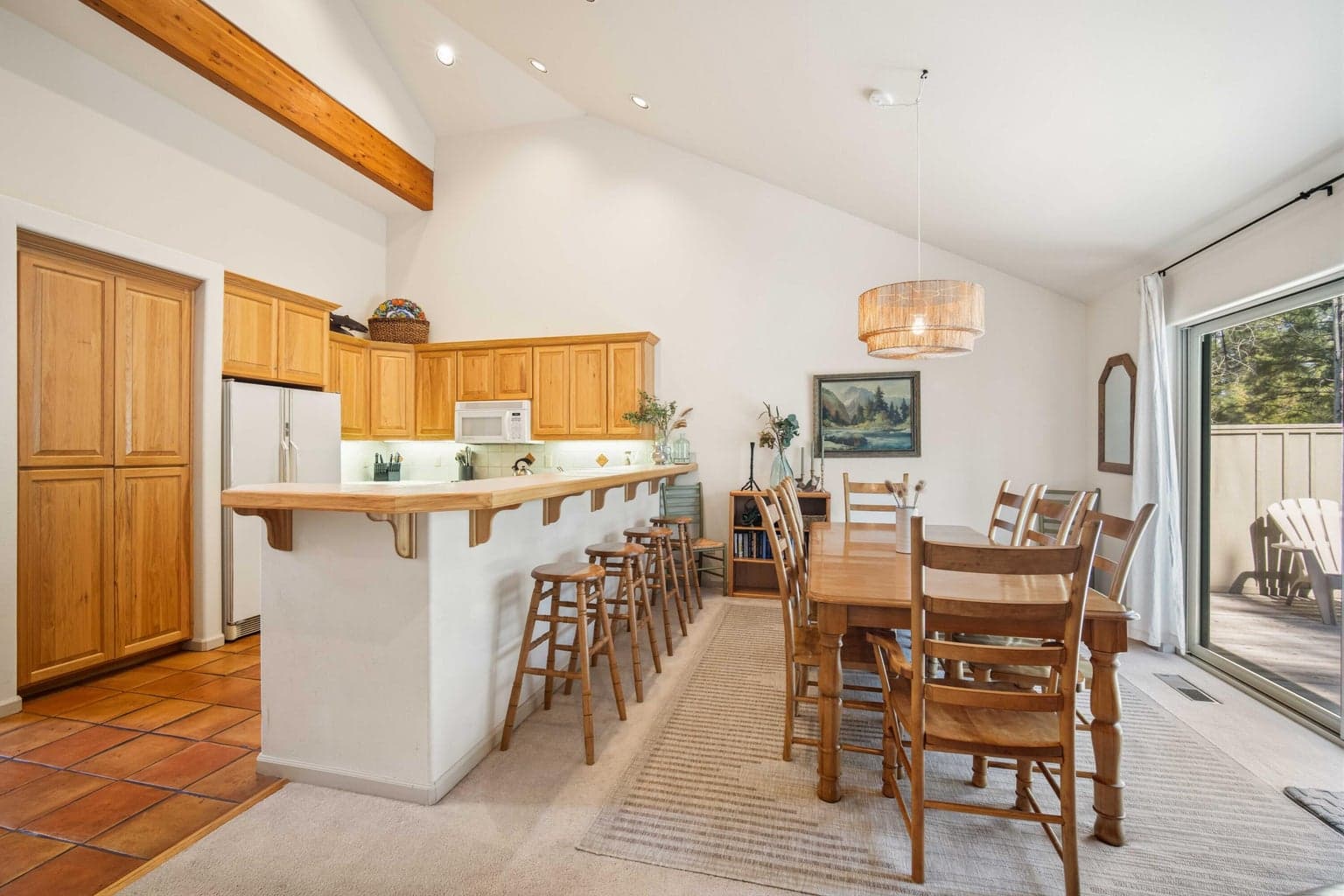 Dining area and kitchen with breakfast bar seating, vaulted ceiling, and nearby sliding door access to the back deck.
